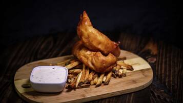 A wooden serving board with a stack of golden-brown fish and a small bowl of white dipping sauce.
