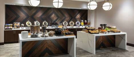 A buffet setup with multiple serving stations, a modern wooden and marble design, and hanging spherical light fixtures.