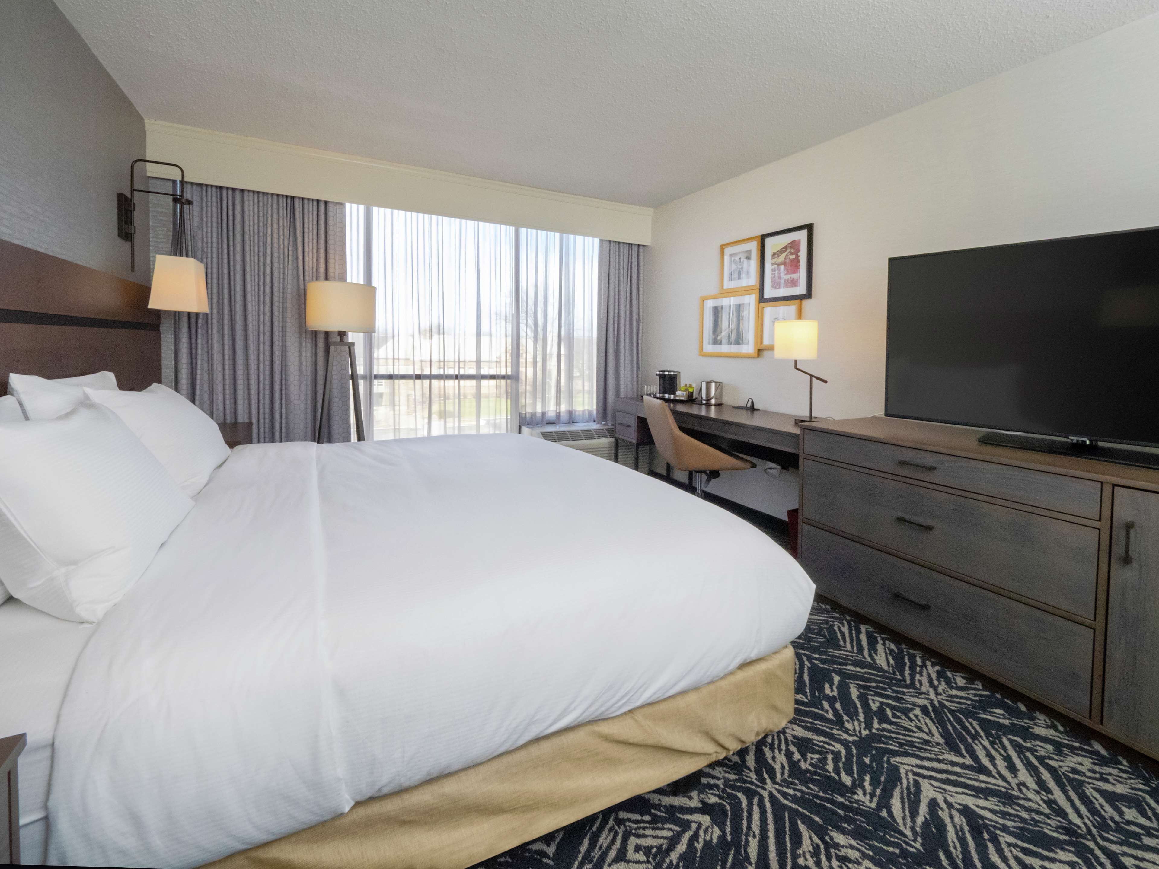 Habitación de hotel con una cama grande, un escritorio, un televisor y una ventana con cortinas.