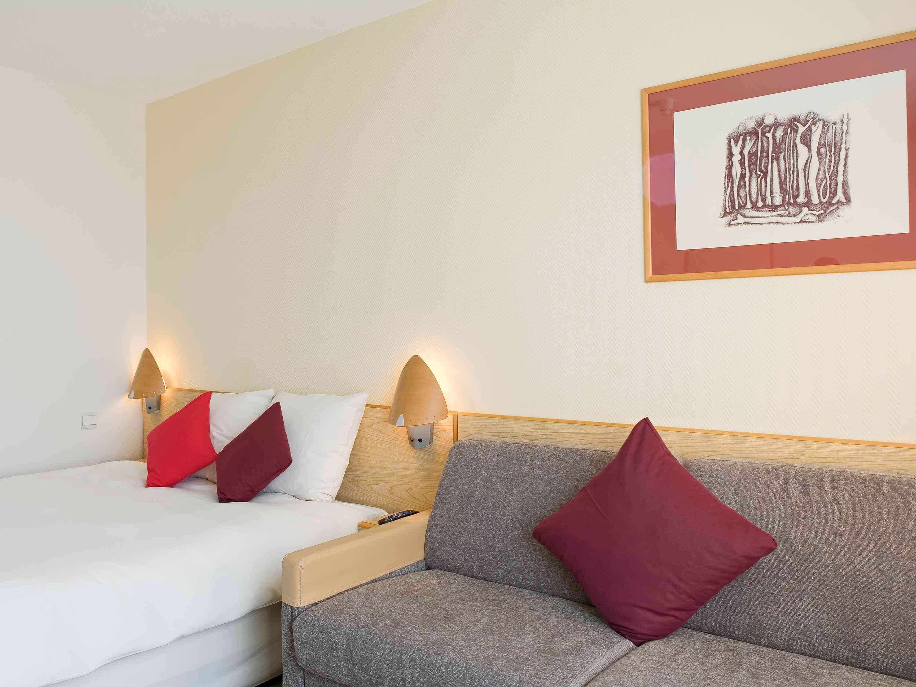 A hotel room with a bed, a sofa, and two wall-mounted lamps.