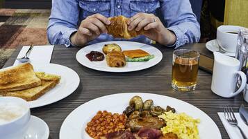 Un desayuno con tostadas, bollería y una variedad de platos que incluyen frijoles, salchichas y huevos revueltos.