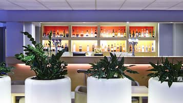 A bar area with multiple shelves of bottles, a bar counter, and several potted plants.