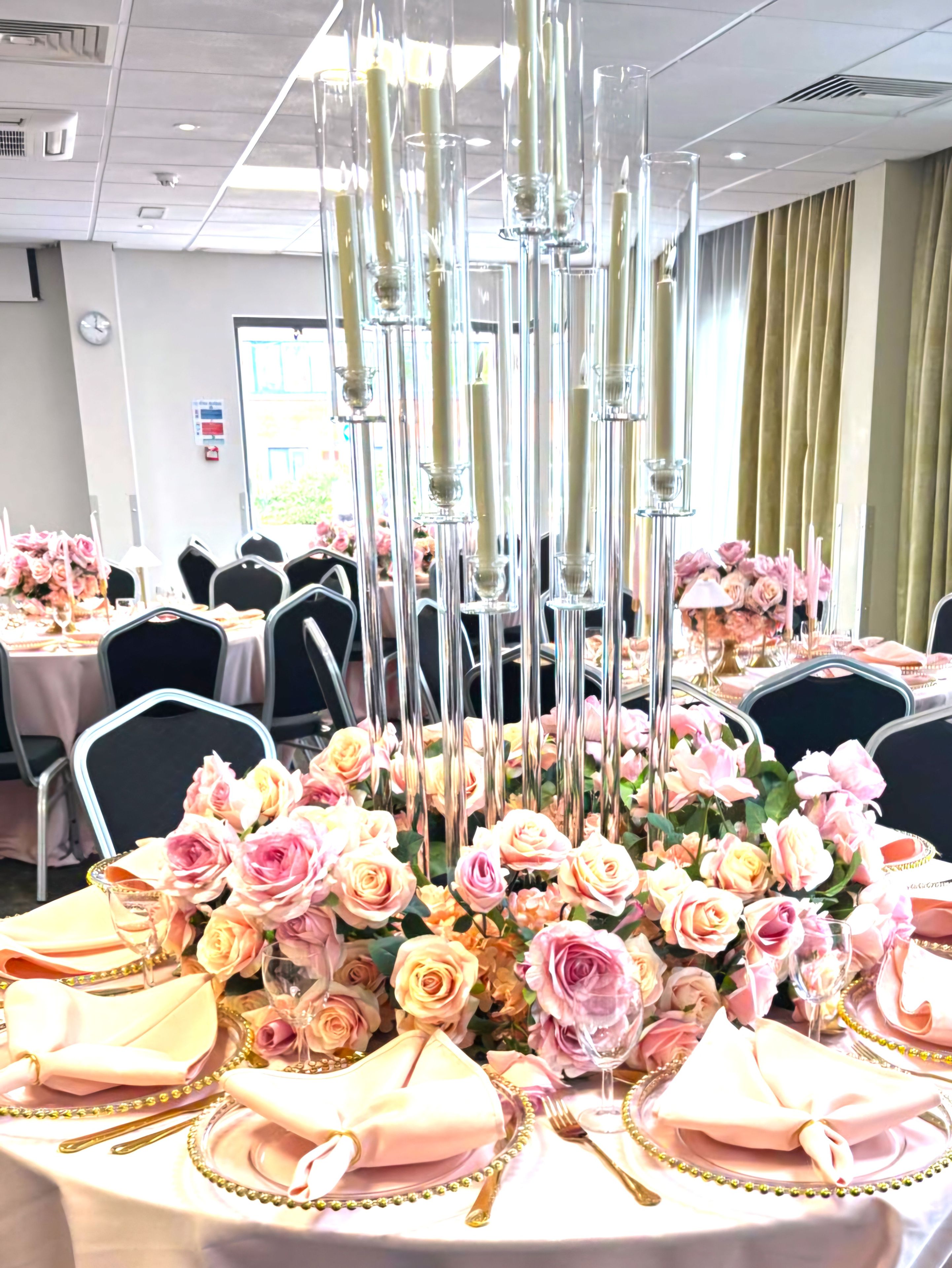 A banquet table with pink roses, clear glass candle holders, and gold detailing.