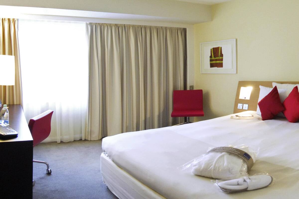 A hotel room with a large bed, a desk with a computer, a chair, and a window with curtains.
