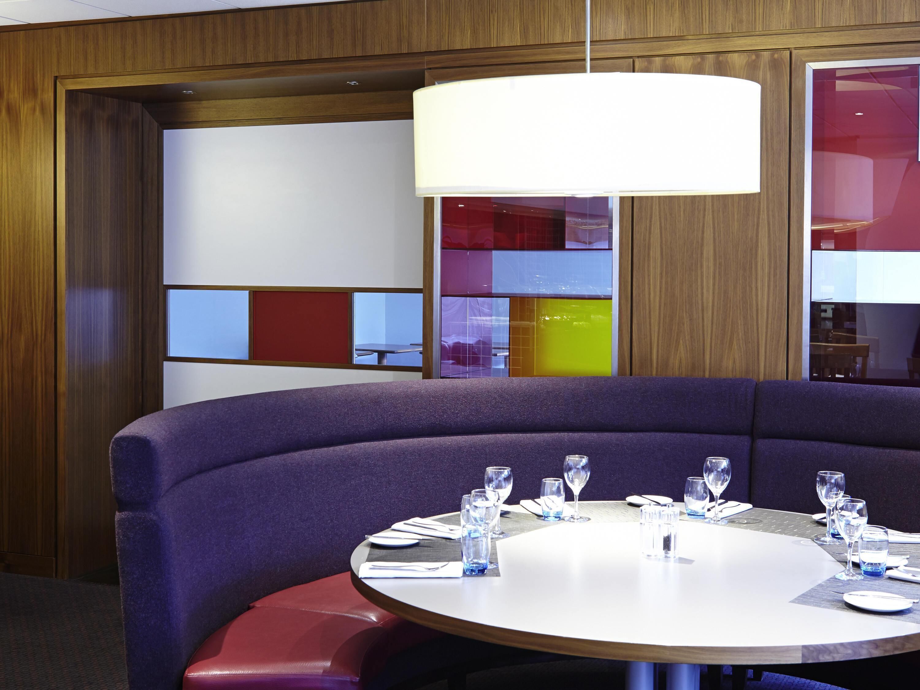 A modern dining area with a round table, purple seating, and a large pendant light.