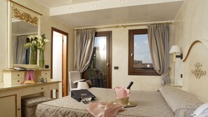A hotel room with a bed, a desk with a mirror, a chair, a bedside table with a lamp, and a window with curtains. - Carlton Capri Hotel (Venice)