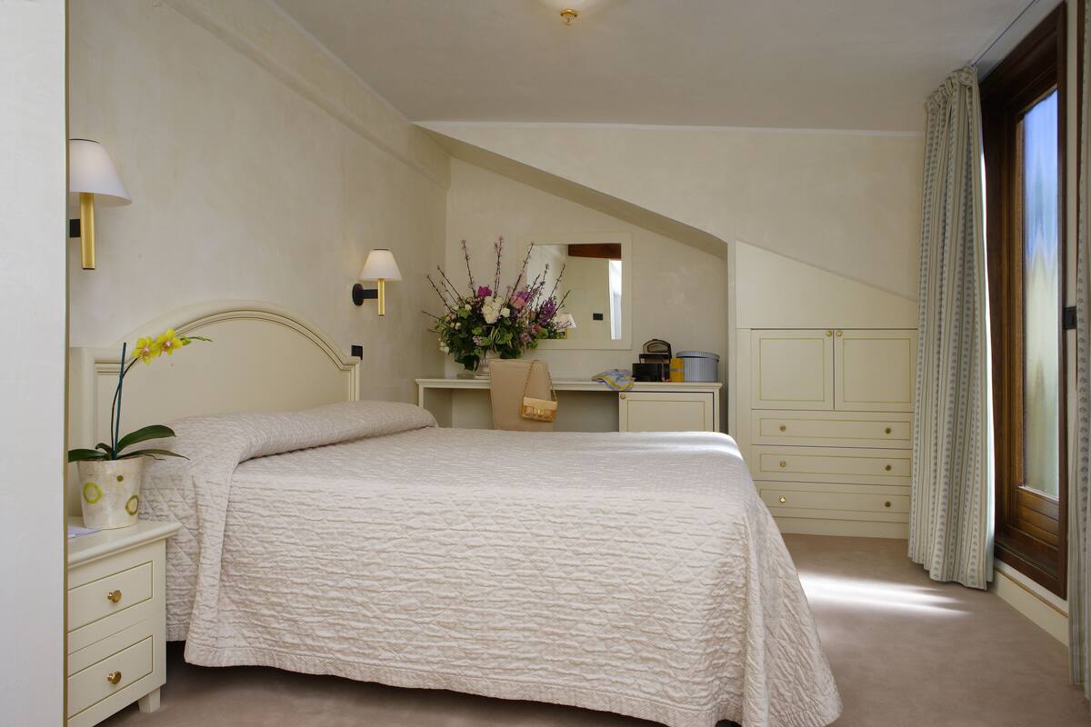 A bedroom with a bed, a nightstand, a dresser, a mirror, a lamp, and a window with curtains.