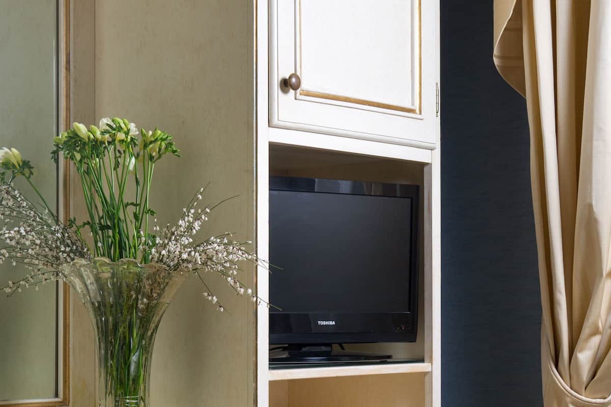 A hotel room with a television on a shelf, a vase with flowers on a table, and a bed with a patterned bedspread.