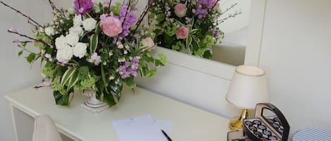 A desk with a vase of flowers, a lamp, and various items including a notebook, pen, and jewelry boxes.