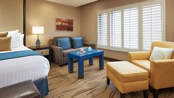 Una habitación de hotel con cama, sofá, mesa de centro y ventana con persianas.