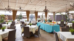 Un vaste espace extérieur aménagé pour les repas, avec de nombreuses tables et chaises, protégé par un toit à motifs géométriques et agrémenté de lustres suspendus.