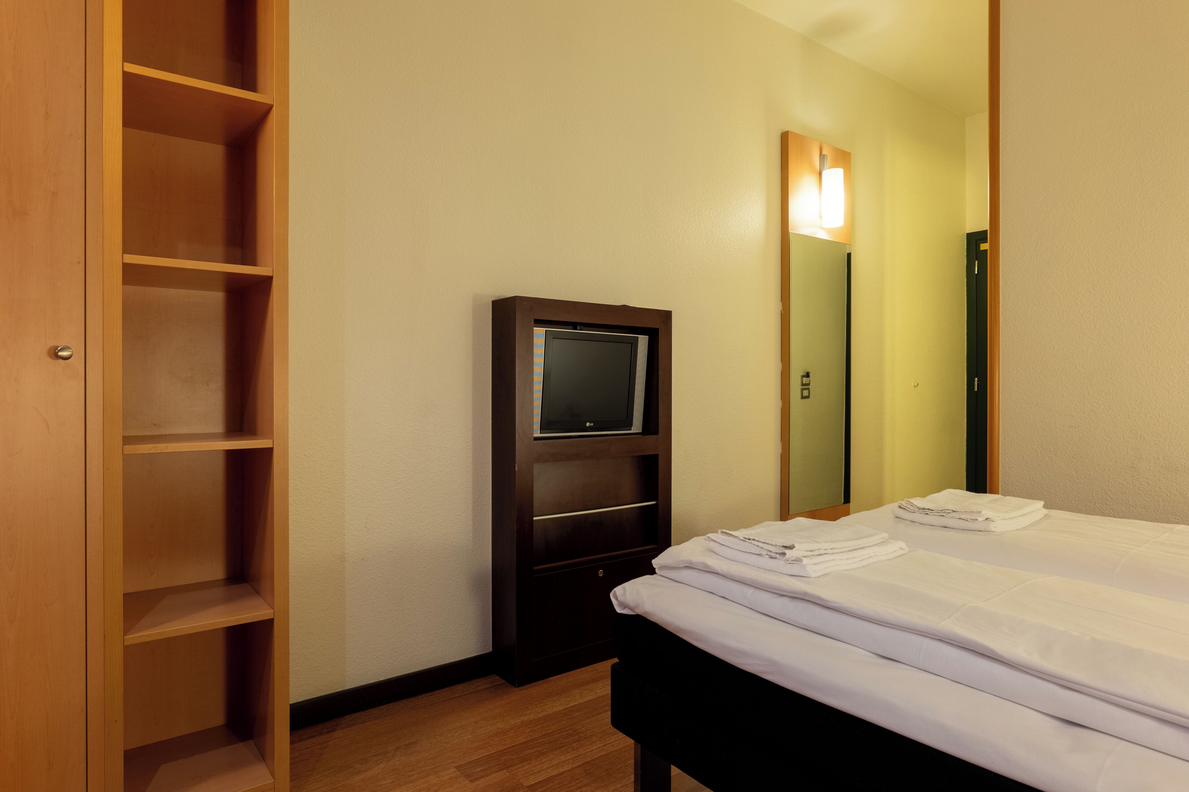 A hotel room with a bed, a TV, and a wooden wardrobe.