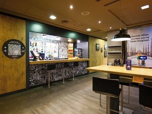 A bar area with a QR code for online orders, a counter with a menu, and a poster advertising Milan. - a&o Hostel Milano Ca Granda (Milan)
