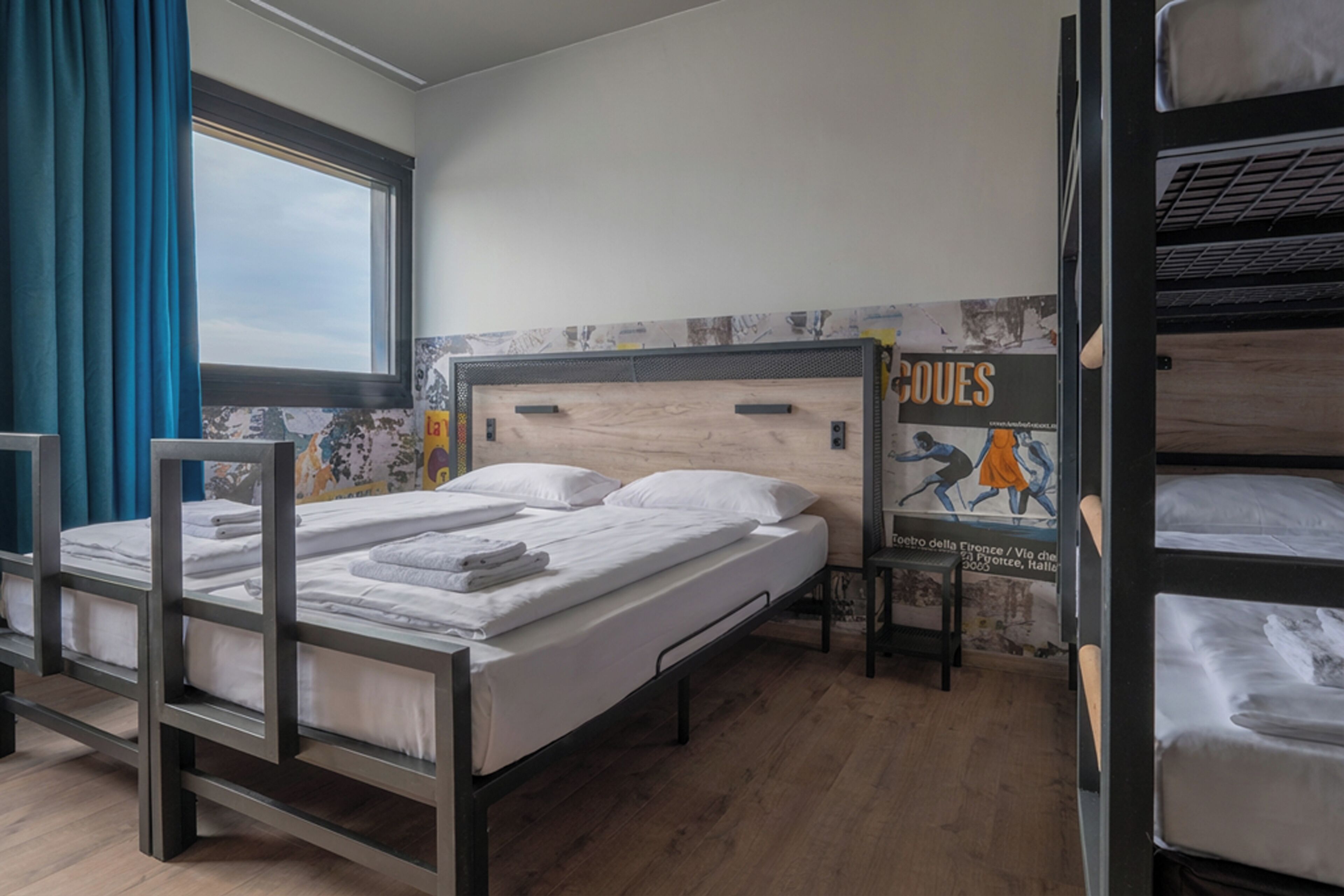 Une chambre de dortoir avec des lits superposés, une fenêtre avec des rideaux et une affiche accrochée au mur.