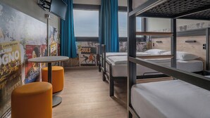 A bunk bed room with a television, a small table, and orange ottomans. - a&o Hostel Milano Ca Granda (Milan)