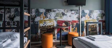 Une chambre d’hôtel avec des lits superposés, un téléviseur à écran plat, une petite table et des affiches accrochées au mur.