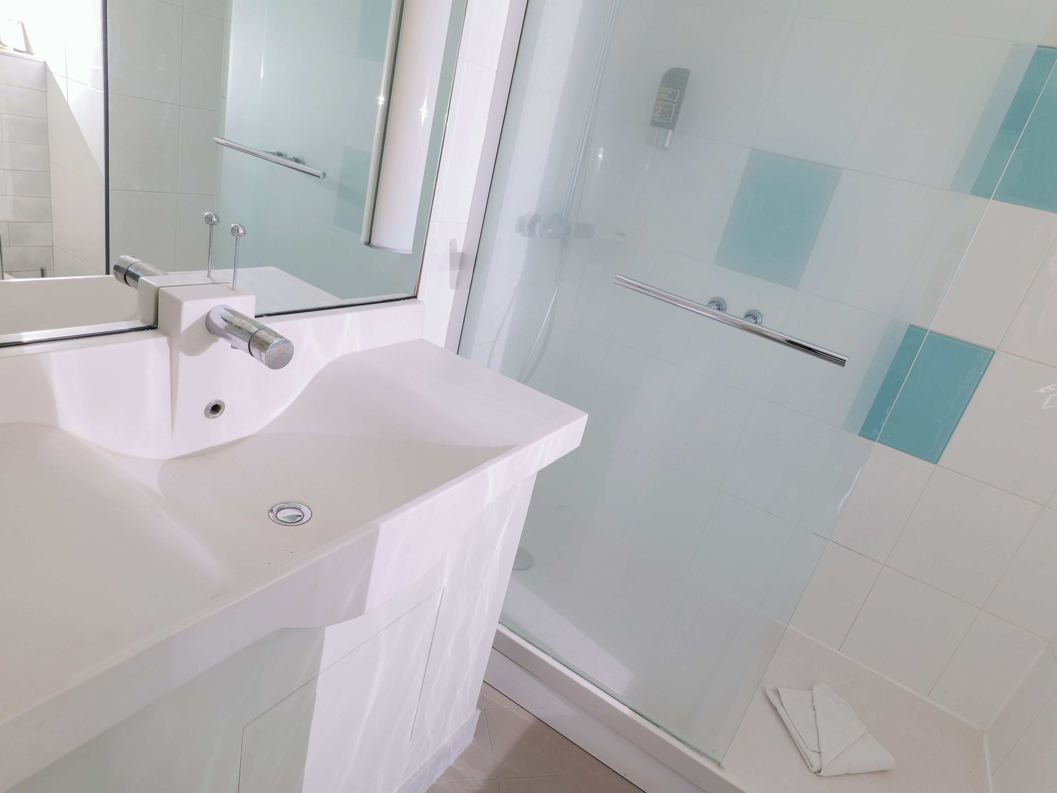 Une salle de bain moderne avec un lavabo blanc, une douche à parois de verre et un miroir.