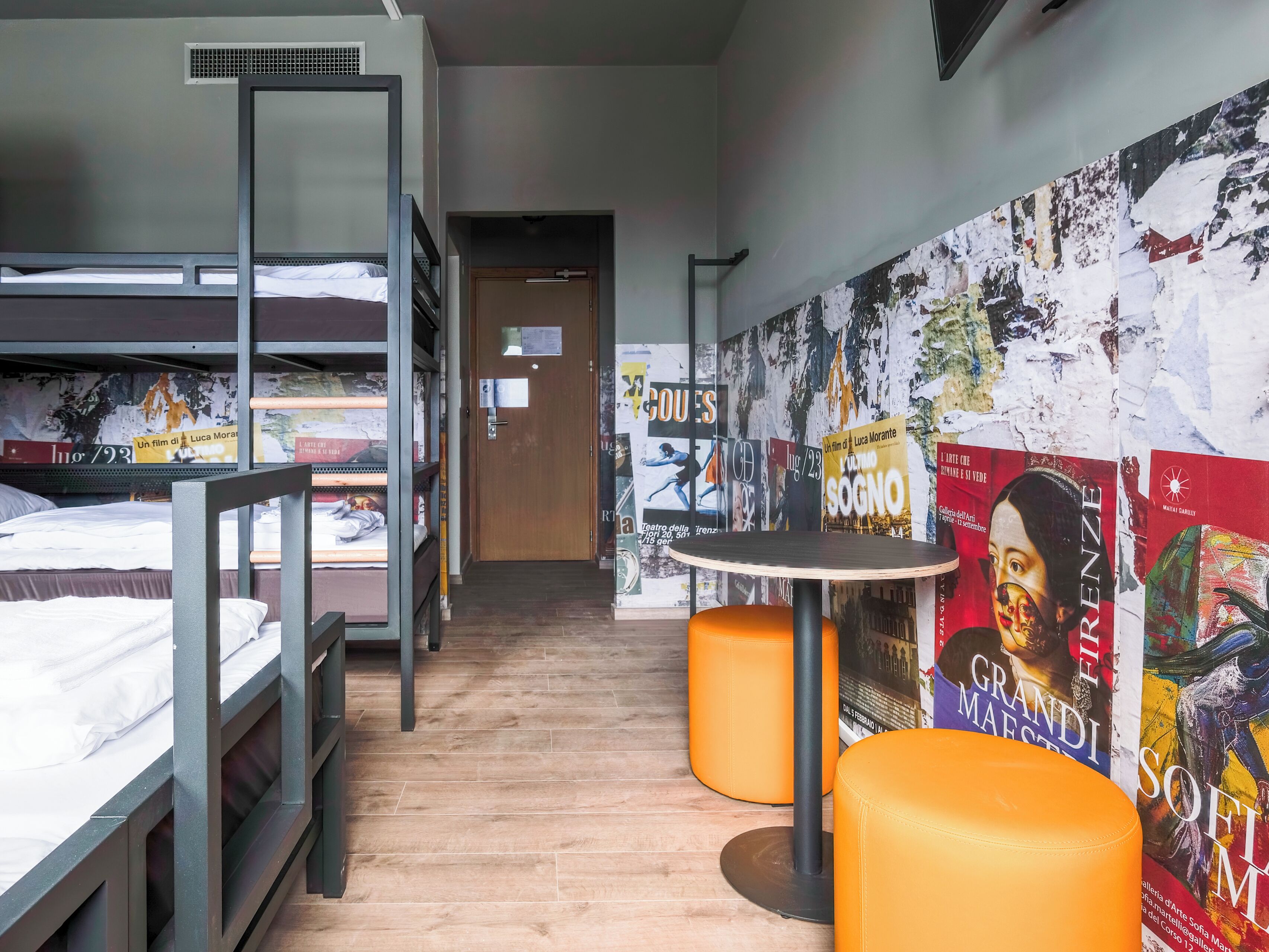 A hostel room with bunk beds, a wooden floor, and a wall decorated with art posters.