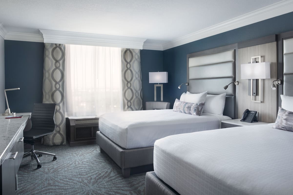 A hotel room with two beds, a desk, and a chair.