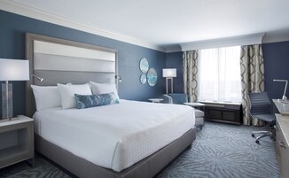 A hotel room with a large bed, bedside tables, a desk, a chair, and a window with curtains.
