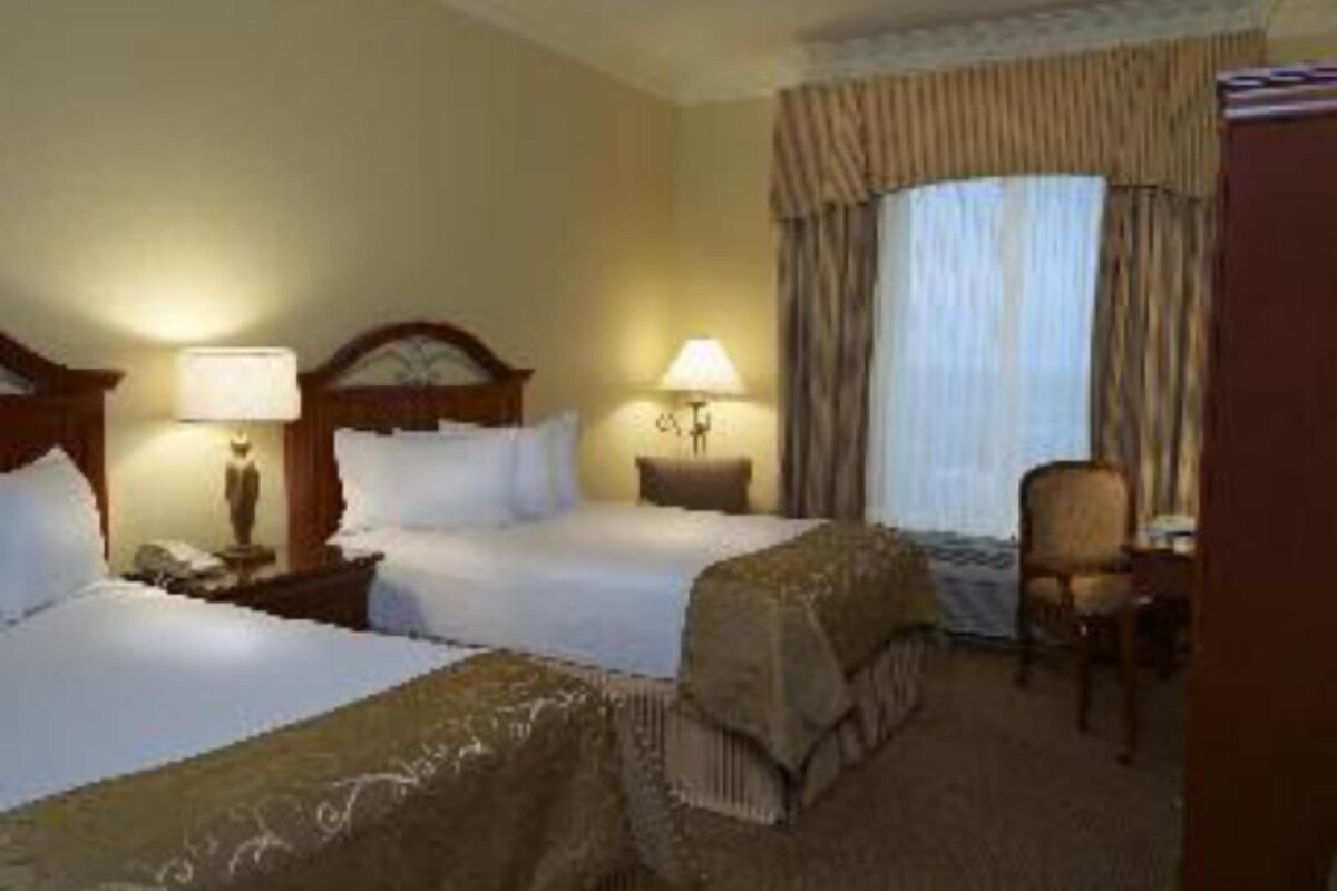 A hotel room with two beds, a chair, a desk, and a window with curtains.