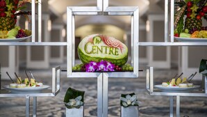 Une présentation de fruits avec une pastèque au centre, étiquetée « CENTRE », entourée de divers fruits et fleurs.