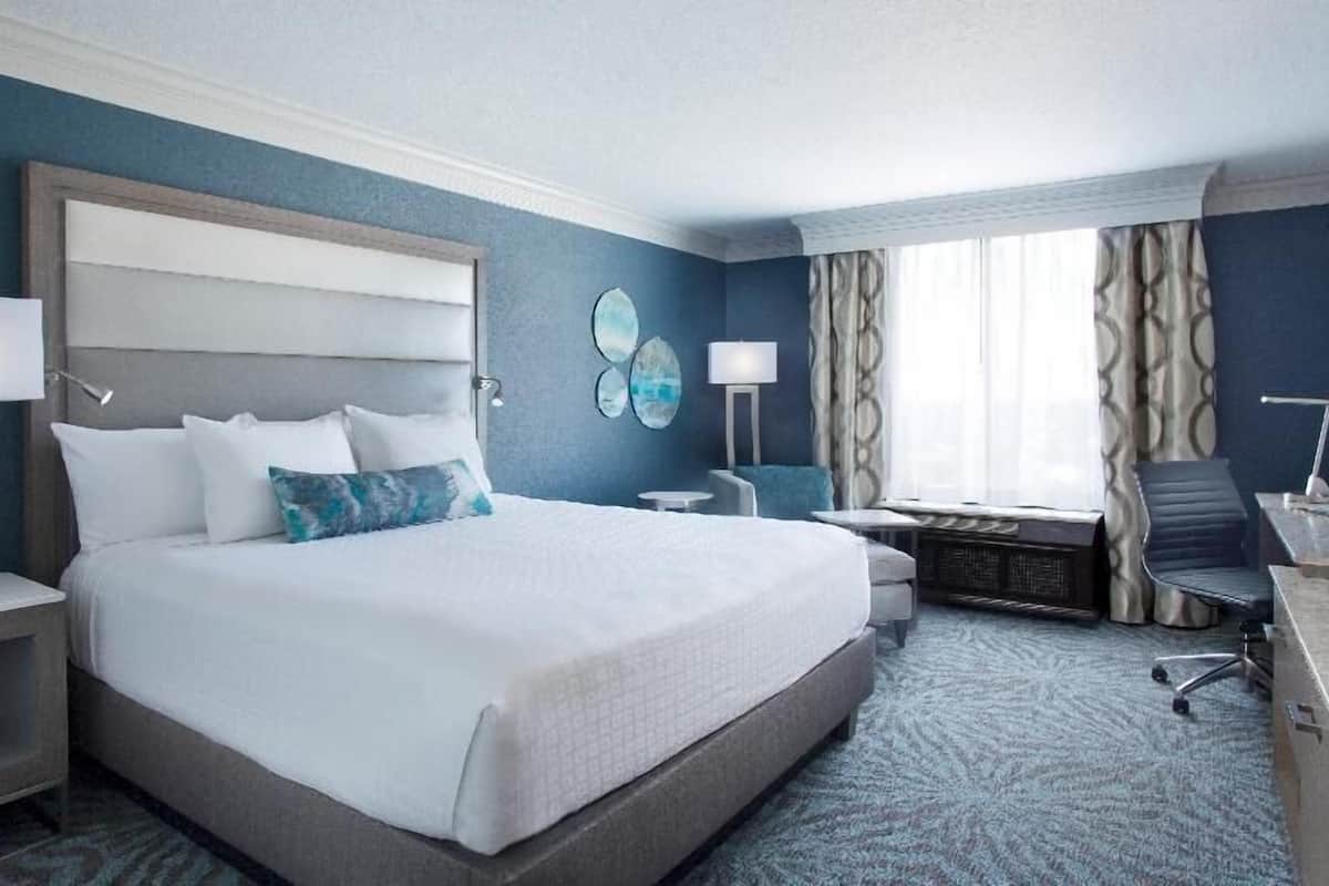 A hotel room with a large bed, bedside tables, a desk, a chair, and a window with curtains.
