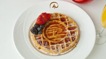 Um prato com um waffle, morangos, mirtilos e um copo de sumo de laranja.