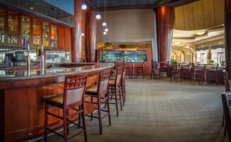 A bar area with wooden bar counters, bar stools, and a large aquarium.