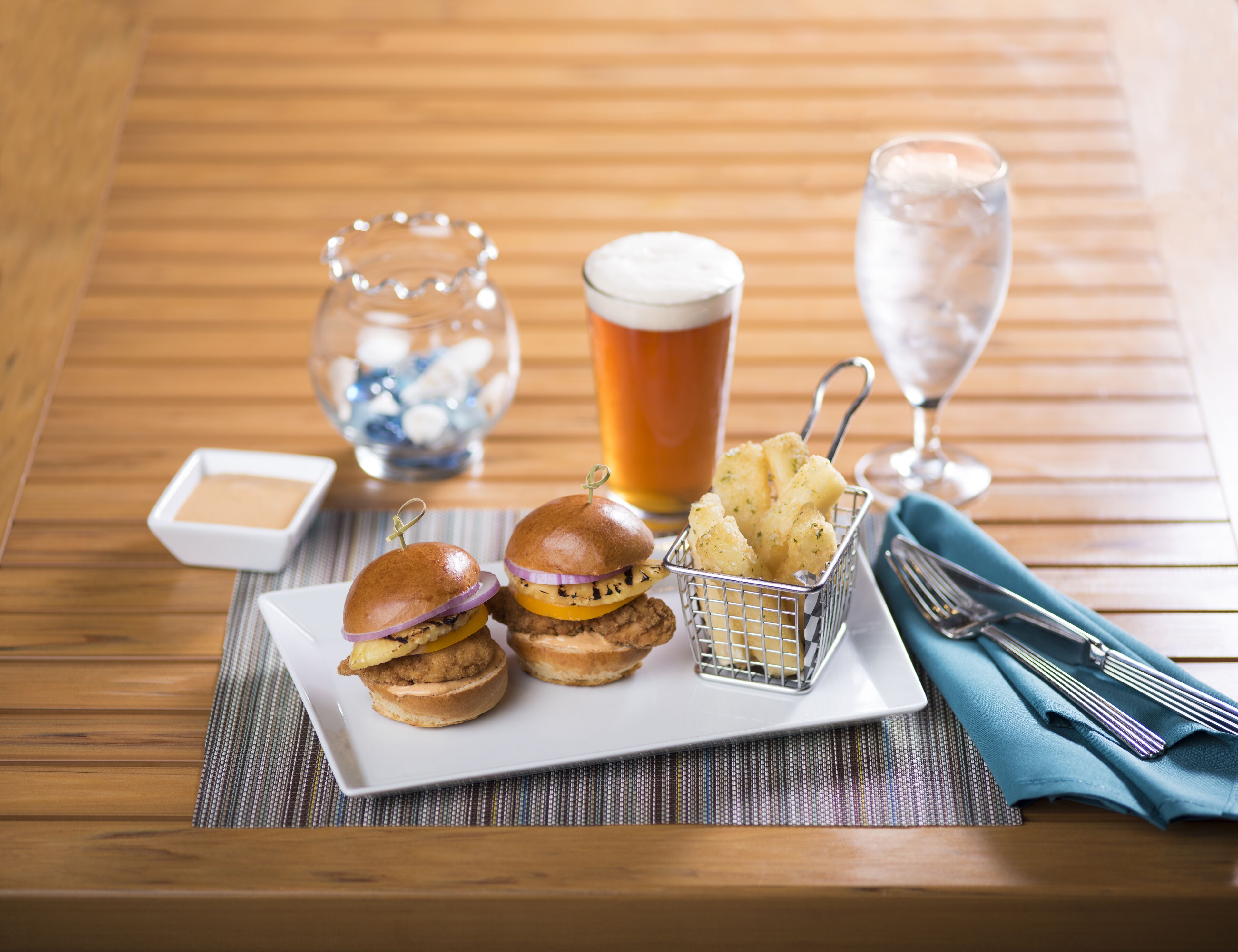 A wooden table with a plate of food, a glass of beer, and a glass of water.