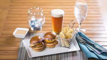 A wooden table with a plate of food, a glass of beer, and a glass of water.