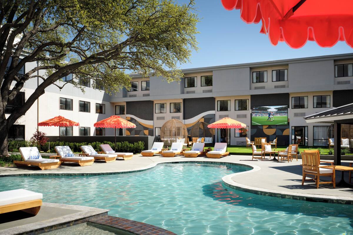 A swimming pool with lounge chairs and umbrellas, a building with multiple windows, and a tree.