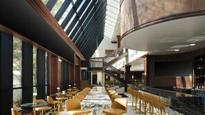A spacious bar area with high ceilings and natural light, featuring a central marble bar and multiple seating options.