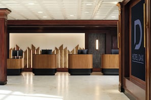 A hotel reception area with a modern design, featuring a reception desk, a wall-mounted sign, and a patterned wall. - Hotel Dax (Addison)