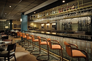 A bar area with a long counter, multiple seating options, and a variety of bottles and glasses on shelves. - Hotel Dax (Addison)