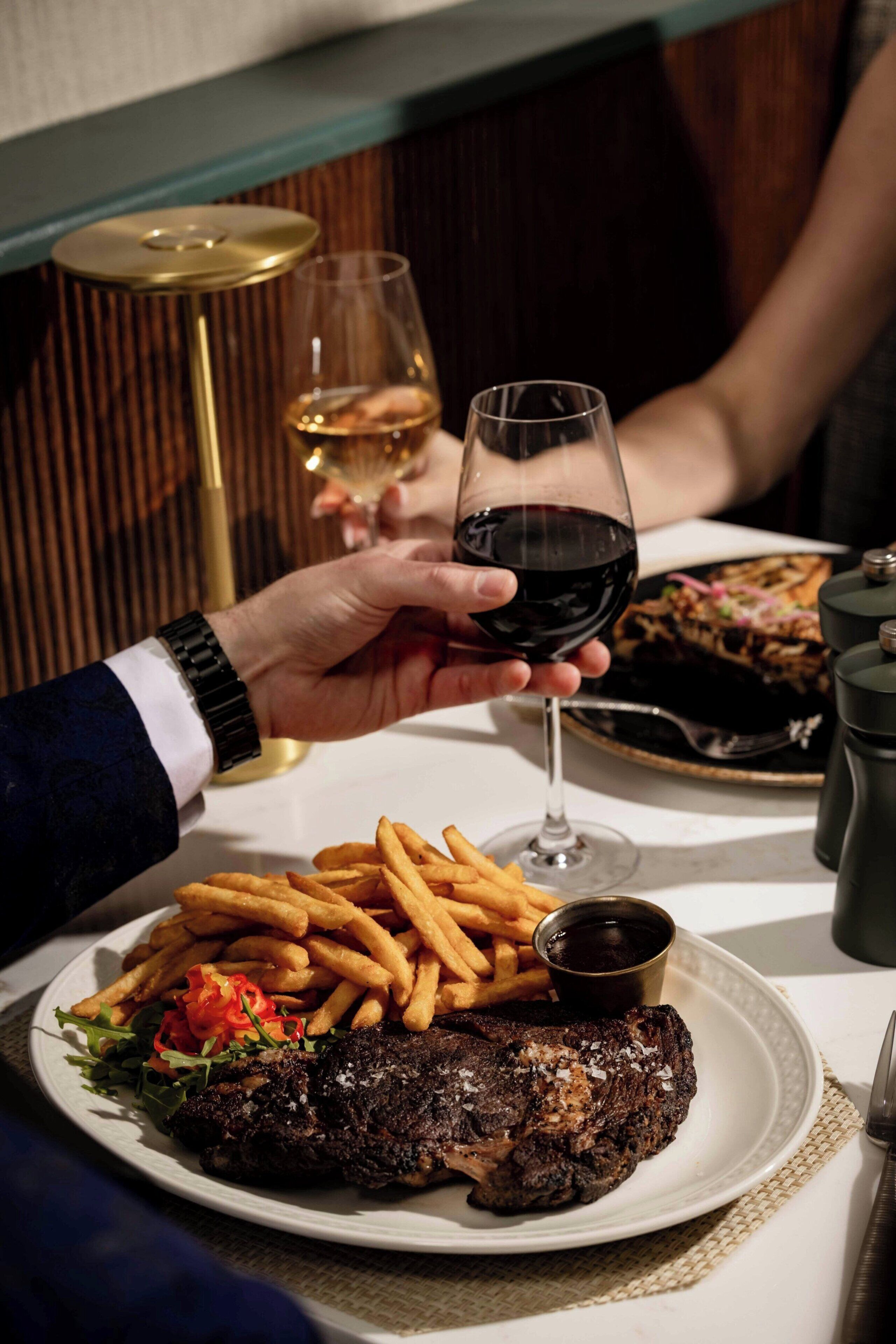 Une table à manger avec une assiette de steak, des frites et une petite coupelle de sauce.