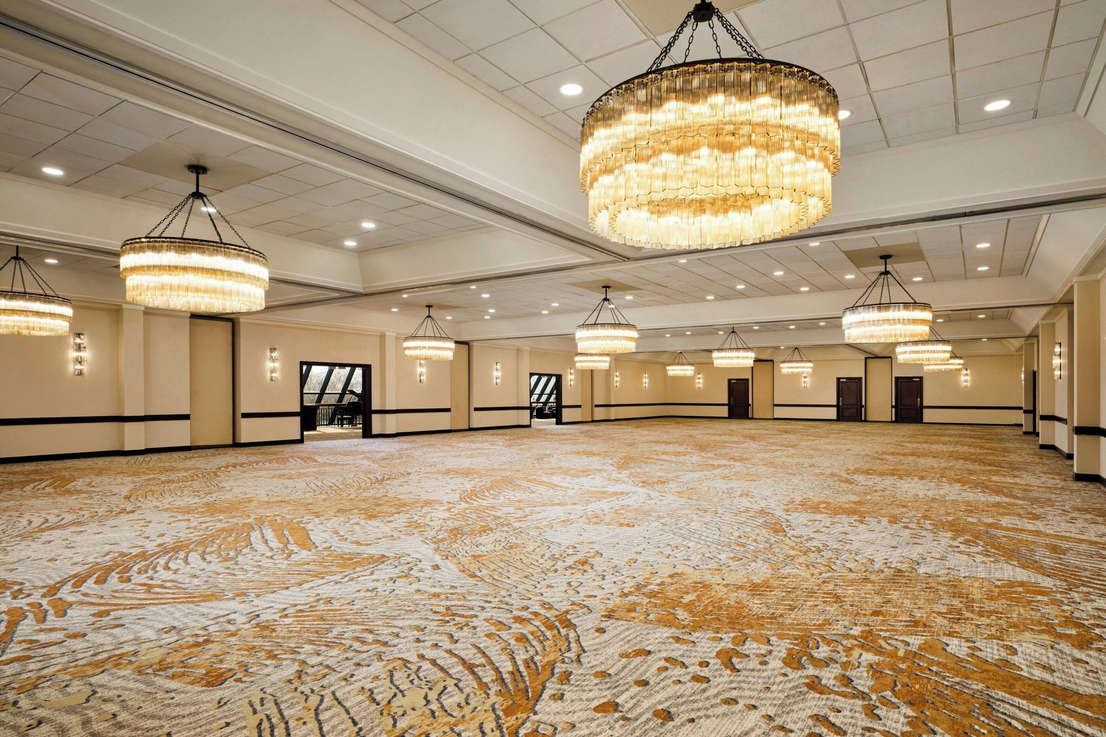 A spacious hall with multiple chandeliers, a patterned carpet, and a neutral color scheme.