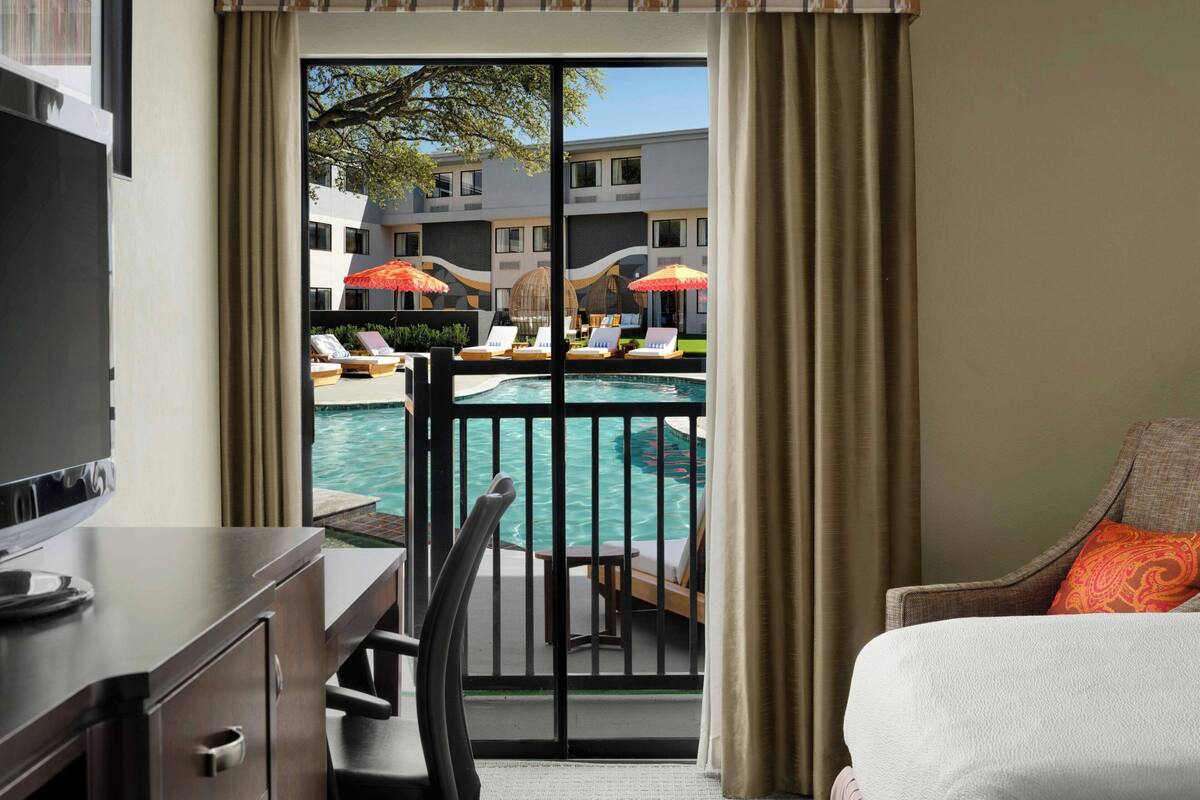 A hotel room with a balcony, a pool, and lounge chairs.
