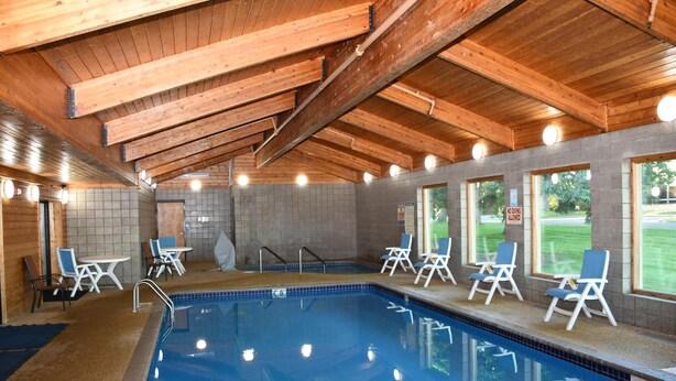 Une piscine intérieure avec des poutres en bois, des murs carrelés et des chaises longues près des fenêtres.