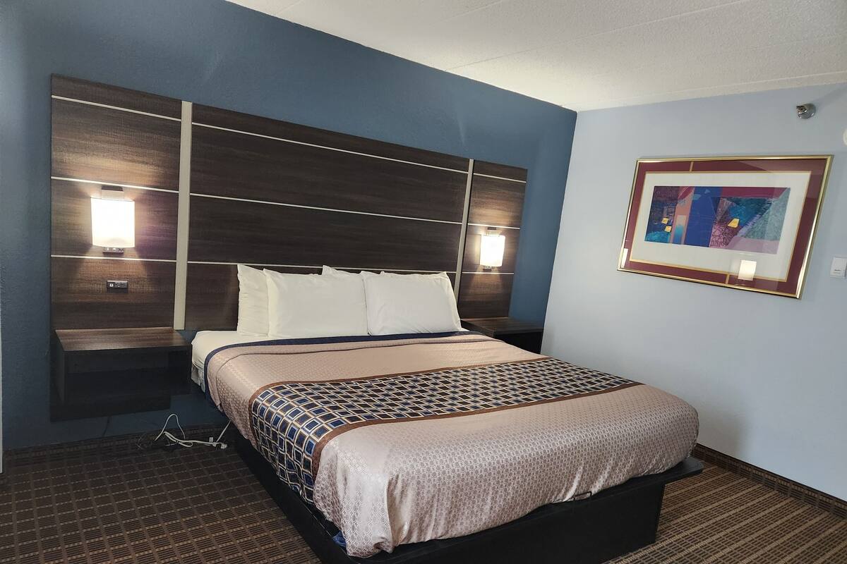 A hotel room with a large bed, a headboard with built-in lighting, a bedside table, and a framed picture on the wall.