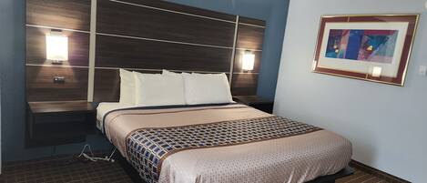 Habitación de hotel con una cama grande, cabecera con iluminación integrada, mesita de noche y un cuadro enmarcado en la pared.