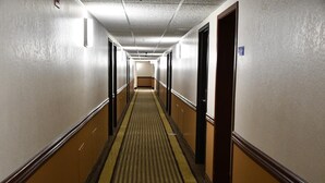 Un long couloir étroit, typique d’un hôtel, avec un tapis à rayures, des portes des deux côtés et un plafond de couleur claire.