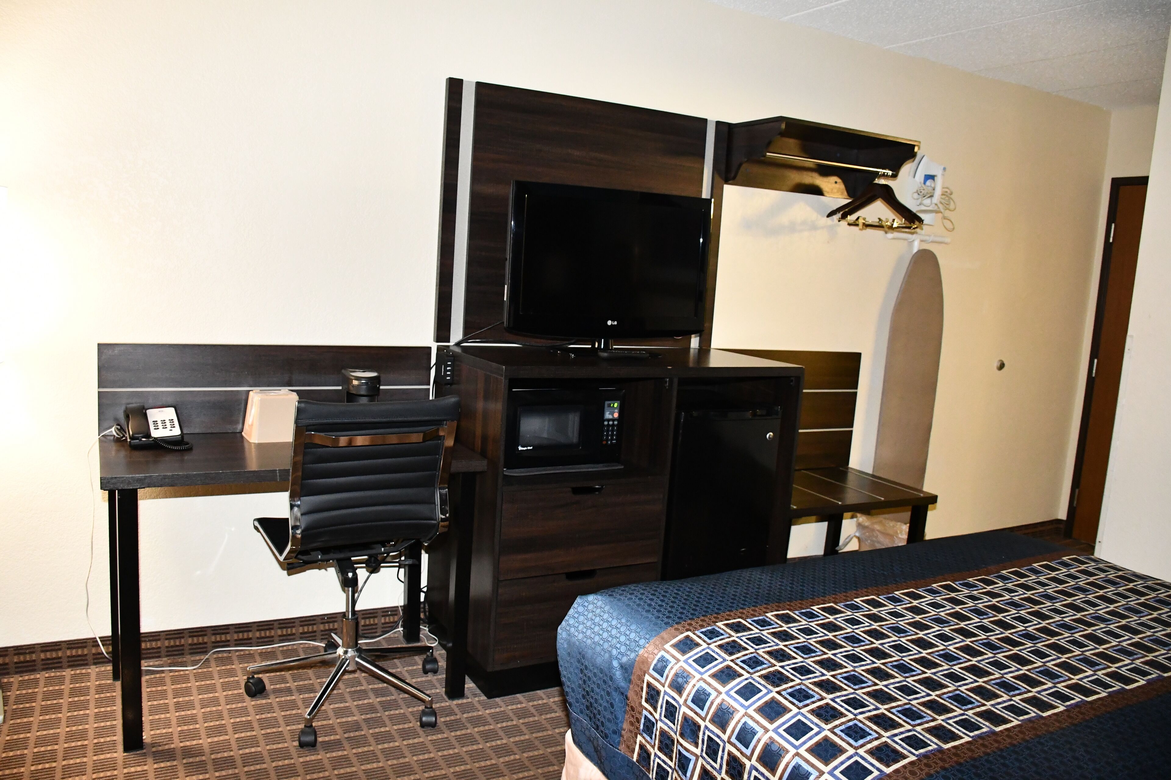 A hotel room with a bed, a desk with a telephone, a microwave, and a television.