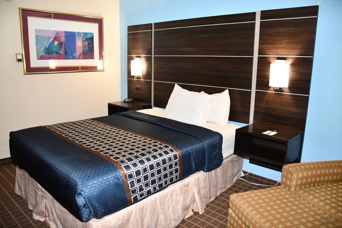 A hotel room with a large bed, two bedside tables, a nightstand, a framed picture on the wall, and a patterned armchair.