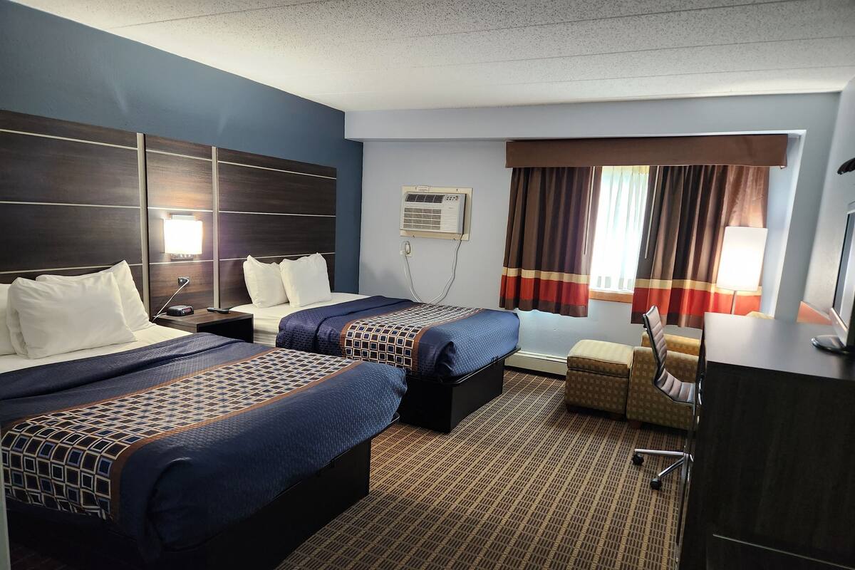 A hotel room with two beds, a desk, a chair, a TV, and a window with curtains.