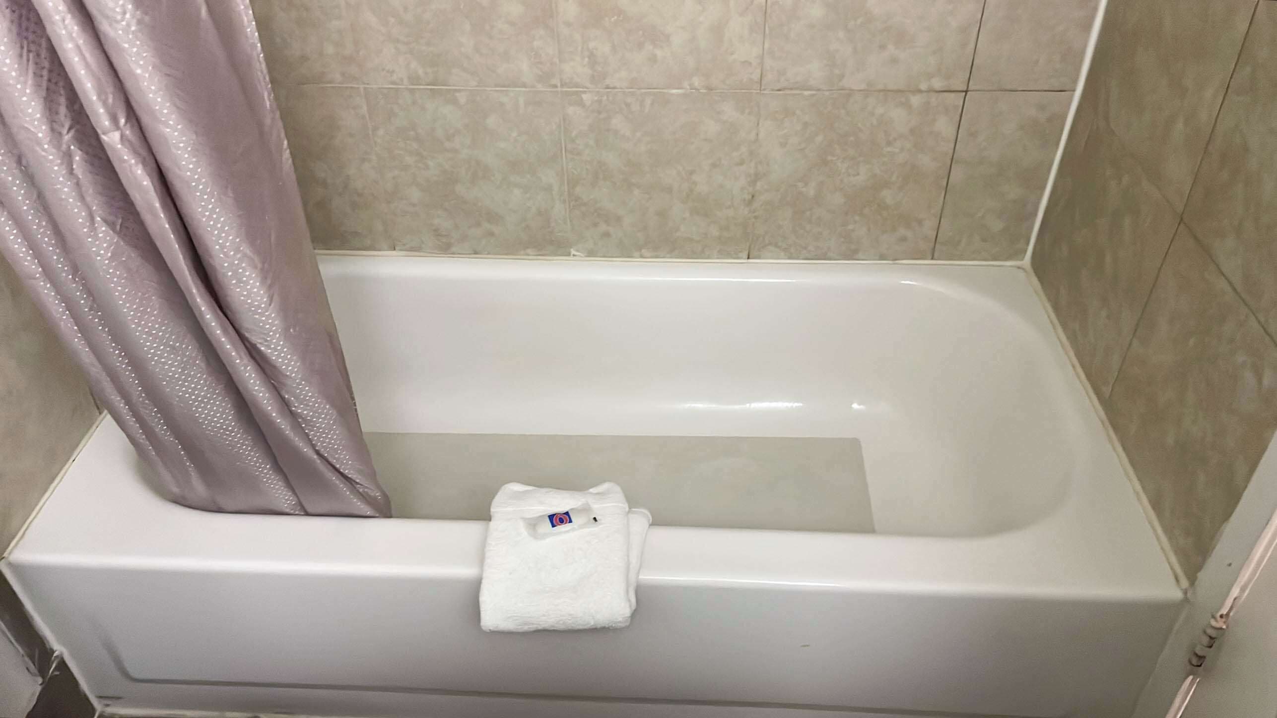 Un bagno con una vasca da bagno bianca, un asciugamano bianco e una tenda da doccia rosa.