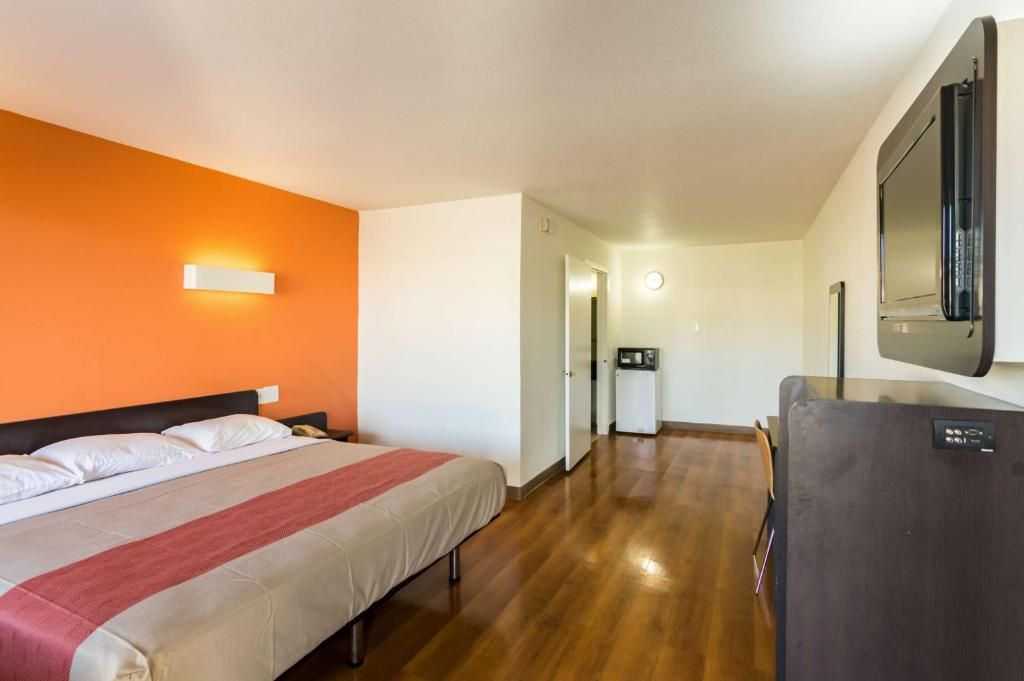 A hotel room with a bed, a desk, a refrigerator, and a wall-mounted TV.