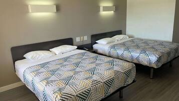Dos camas individuales con ropa de cama estampada, un cabecero oscuro y una lámpara fijada a la pared.