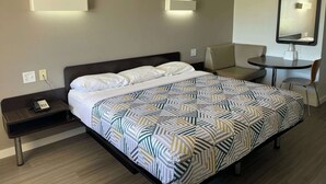 Ein Hotelzimmer mit einem Bett, einem Nachttisch mit Telefon, einem kleinen Tisch mit Stuhl und einem wandmontierten Spiegel.
