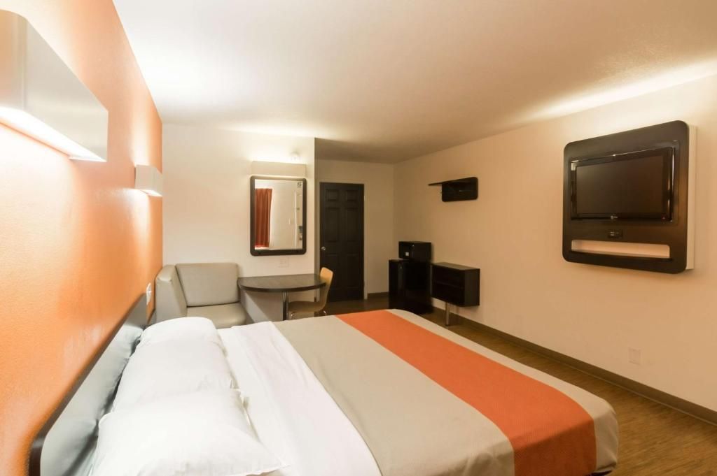 A hotel room with a bed, a desk, a chair, a TV, and a mirror.